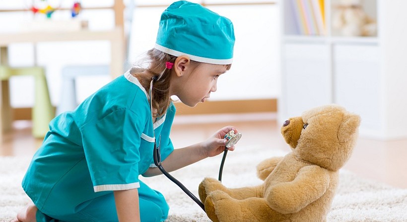 Kind spielt Ärztin und untersucht einen Teddybären auf Blinddarmentzündung.
