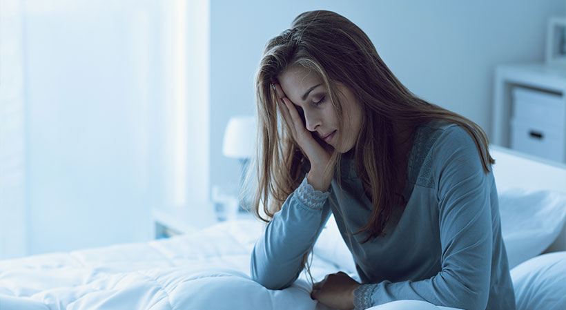 Frau sitzt im Bett und kann nicht schlafen.