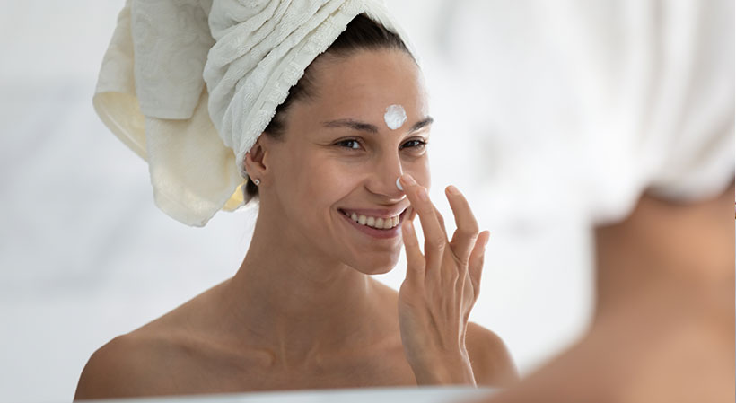 Frau cremt ihr Gesicht mit Sonnencreme ein
